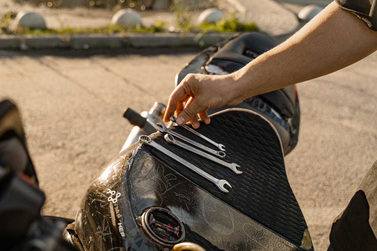 Close-up of a man's hand arranging wrenches on a motorcycle seat outdoors.